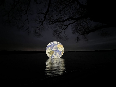 Luke Jerram's art installation, Floating Earth, illuminated at night as it hovers over Pennington Flash in Wigan