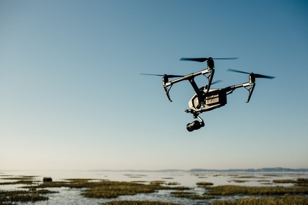 A drone hovering over what looks like a saltmarsh or peatland landscape, against a blue sky