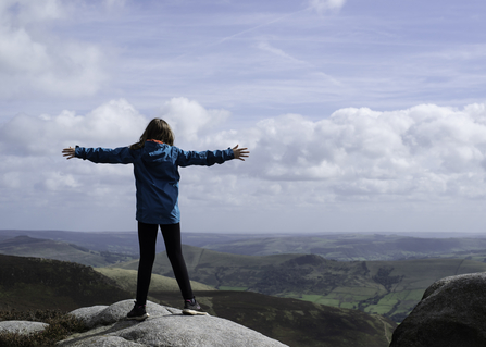 A woman standing on top of a rock with her arms outstretched