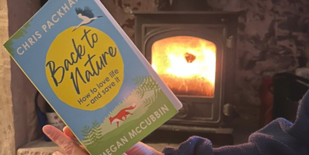 A close up of the book Back to Nature by Chris Packham and Megan McCubbin, being held by someone with a fireplace in the background.
