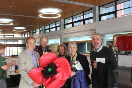 A  group of trustees smiling in a group whilst holding a giant poppy