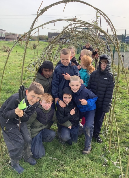 A group of children in a group underneath their handmade willow archway