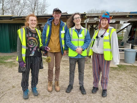 Four people in high-vis smiling at the camera in front of a wooden shelter