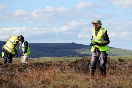 Three people on a moorland with Darwen tower in the background