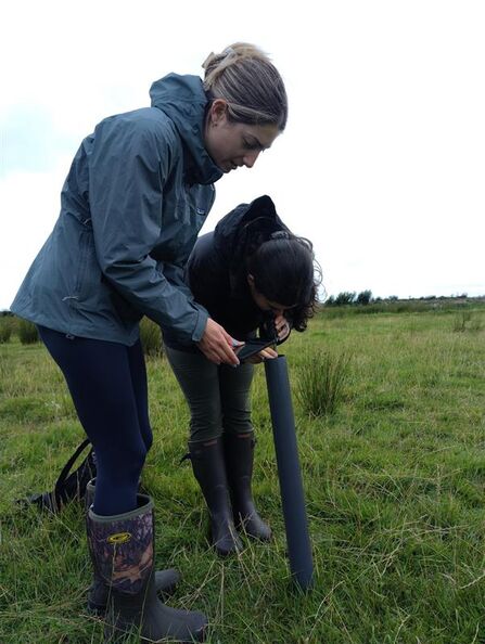 Two women looking into a black pvc pipe