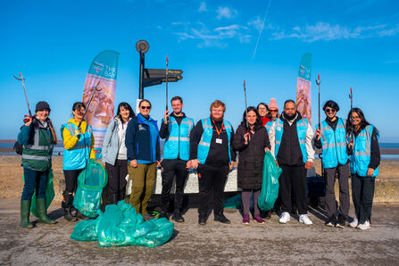 12 people stand with their backs to the beach holding litter pickers and bags of rubbish