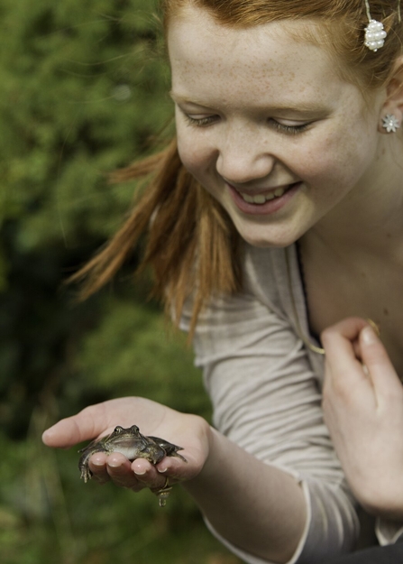 A teenaged girl holding a frog in her hand and smiling