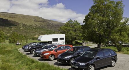 Cars parked at a nature reserve car park surrounded by trees and hills