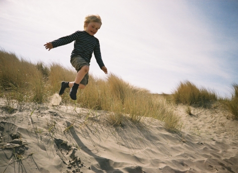 A boy at Beach School leaping down a sand dune on the coast