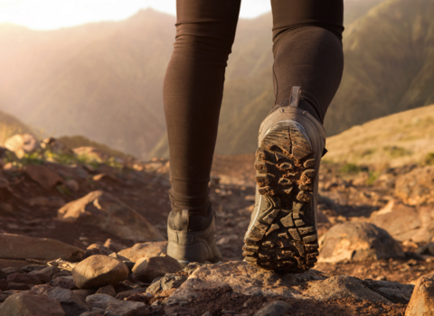 The legs and feet of someone hiking across rugged mountain terrain