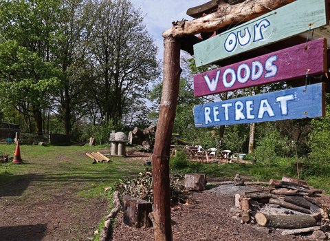 A wooden shelter in a park with a sign saying 'Our Woods Retreat'