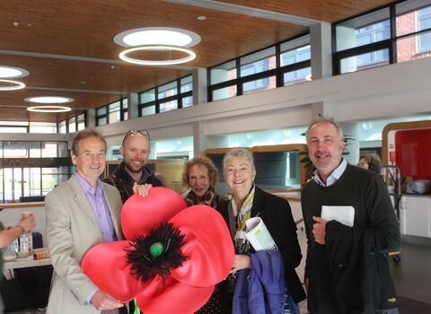 A  group of trustees smiling in a group whilst holding a giant poppy