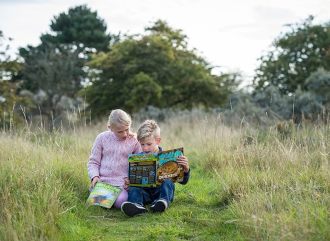 Two children sitting on some grass reading Wildlife Watch magazines.