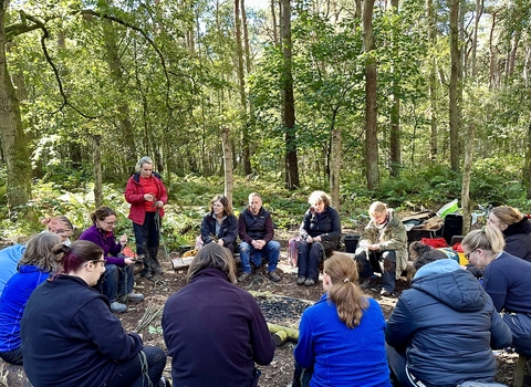 Forest School trainees doing woodland crafts around the fire circle