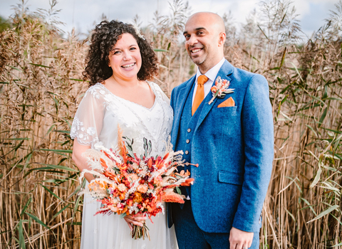 A bride and groom smiling whilst stood in front of reedbeds