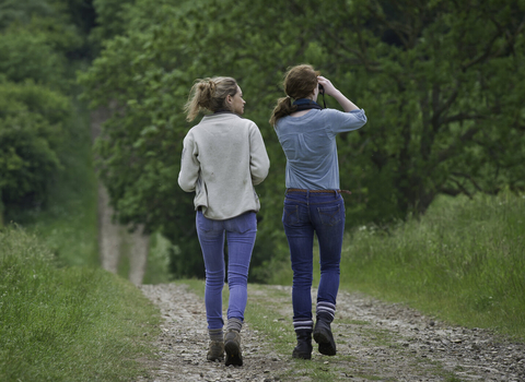 Two women walking down a country lane and looking through binoculars
